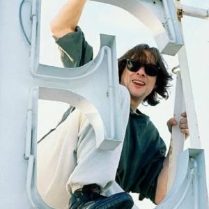 Singer Shaun Ryder of the Happy Mondays climbs on the letter E from a sign on the roof of the Hotel Subur Maritim, where the group are making a video for their single, 'Step On', Sitges, Spain, March 1990. (Photo by Kevin Cummins/Getty Images)